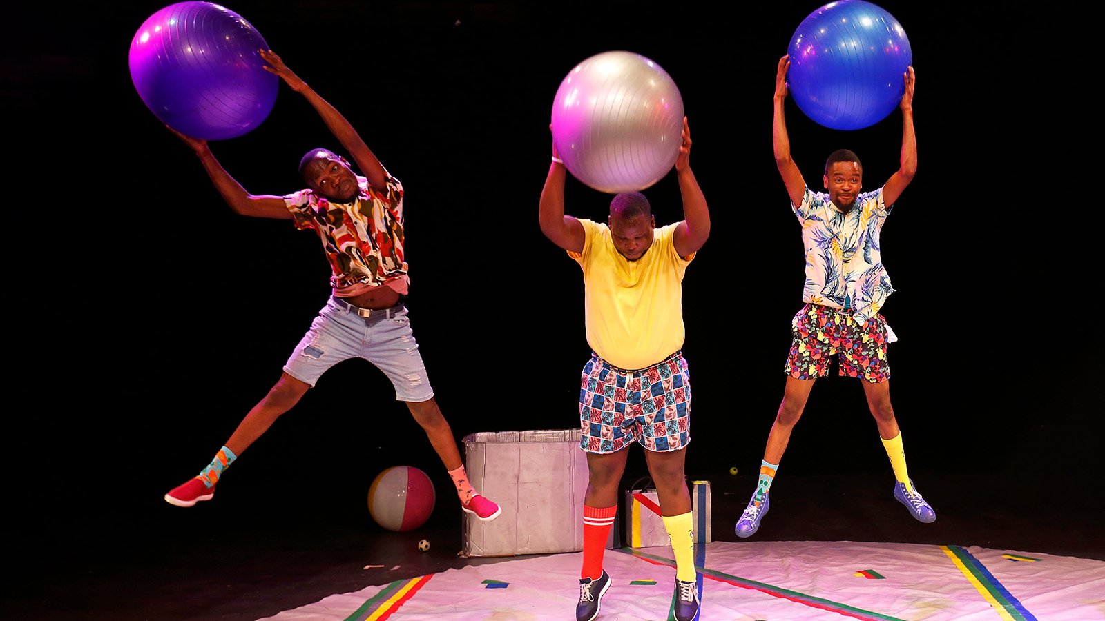Three acrobats holding bouncy balls jump in the air