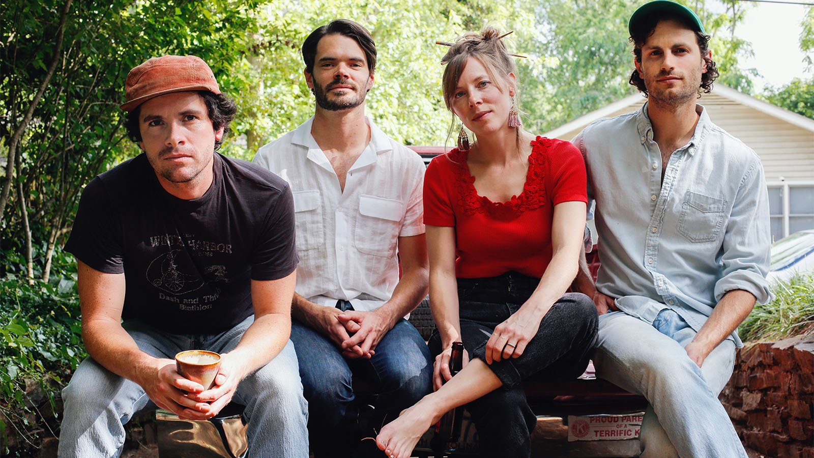 Four band members pose in front of a house