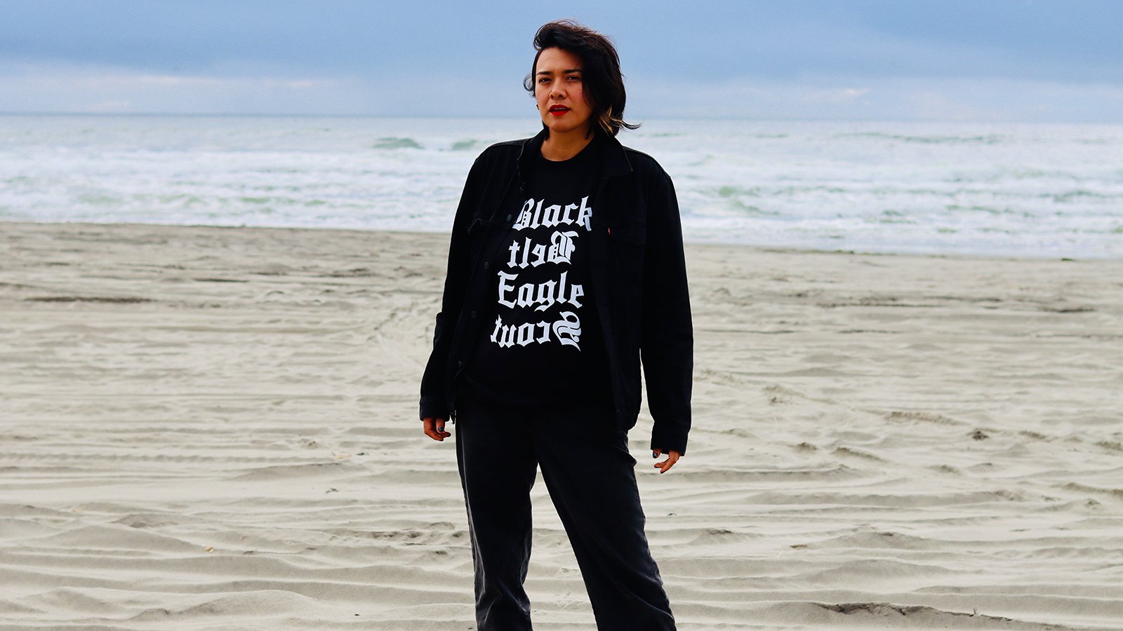 A woman with short brown hair wearing black clothing standing on the beach