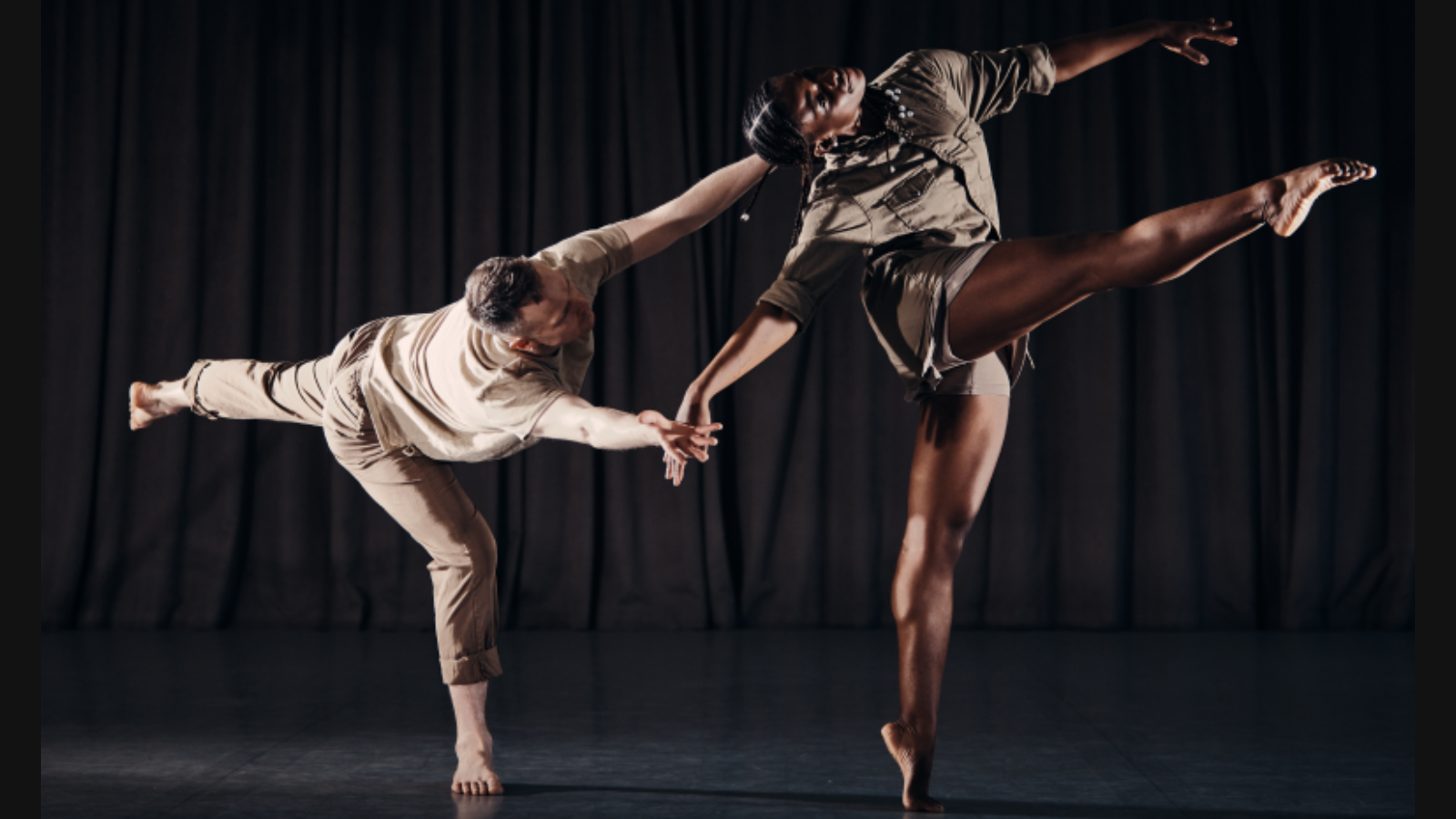 Two dancers and brown clothing in front of a black curtain