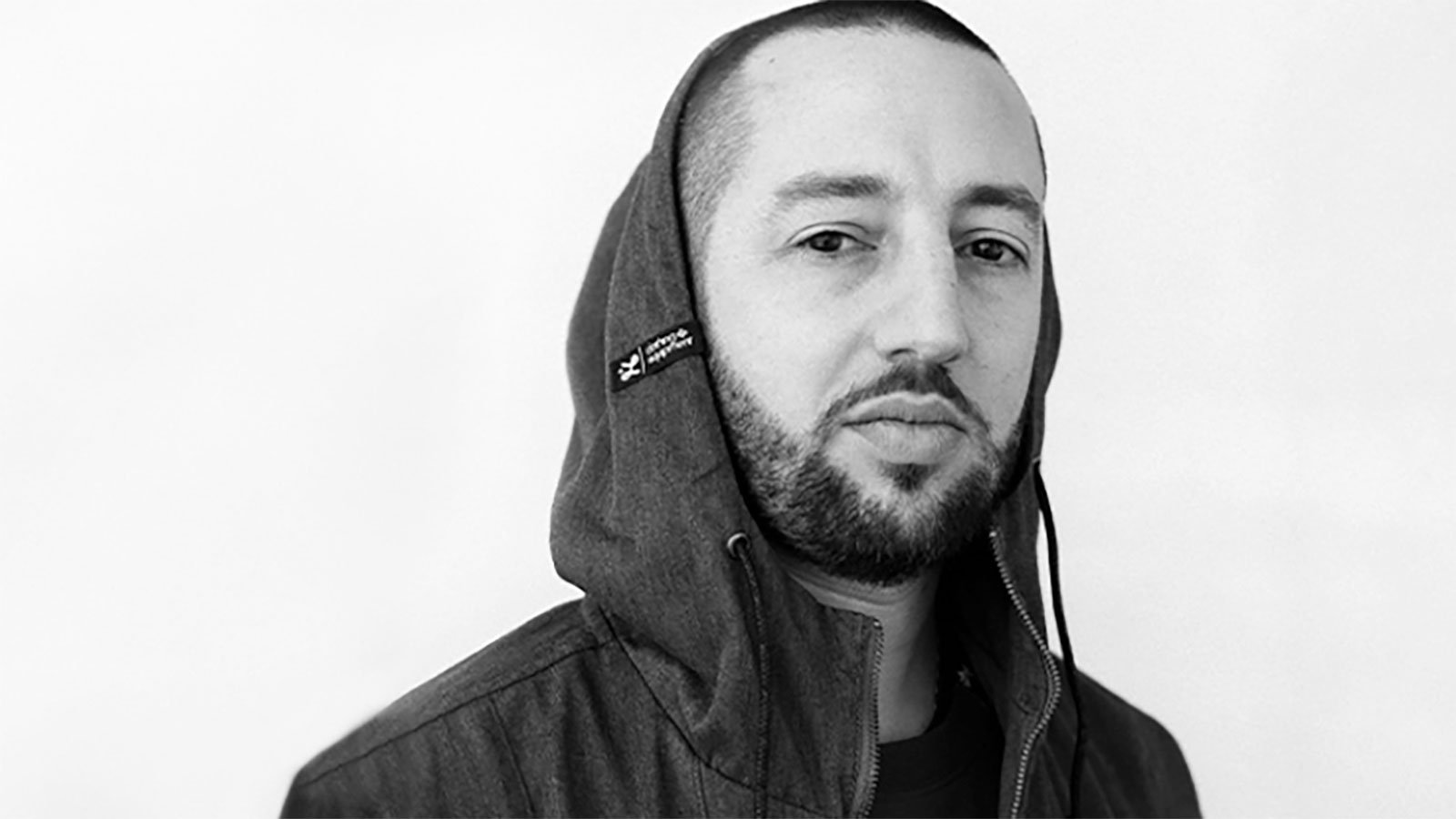 Black and white photo of a man with a buzz cut wearing a hoodie jacket