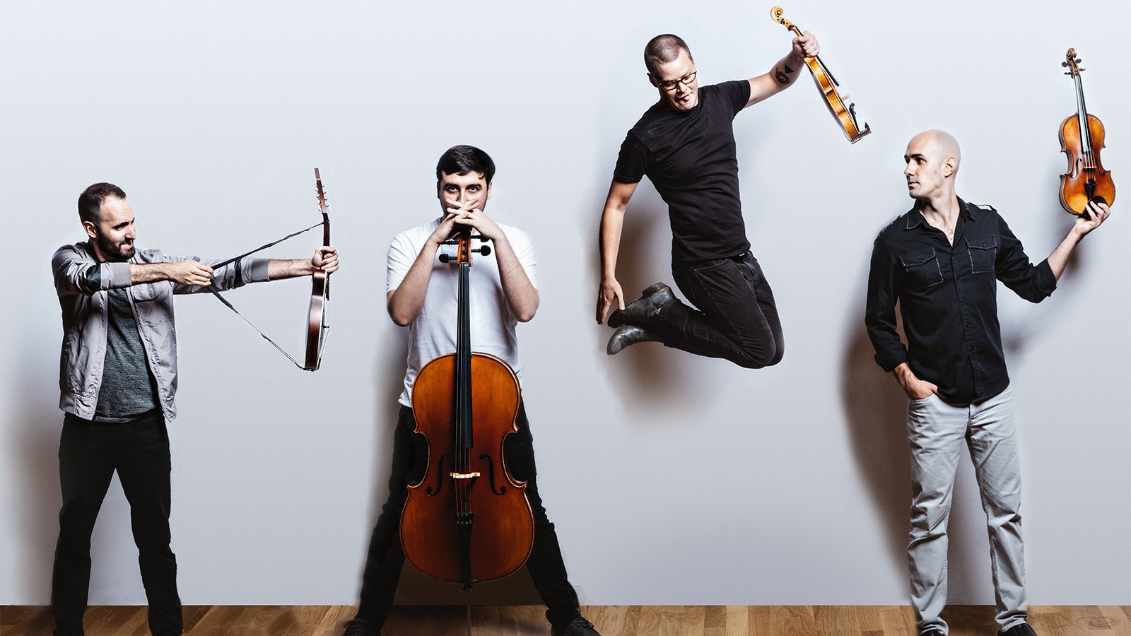 Four men posing with their instruments in front of a white wall