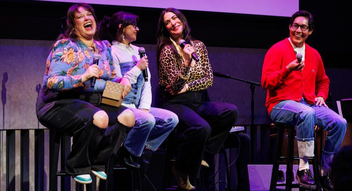 Four people sitting on stools laughing
