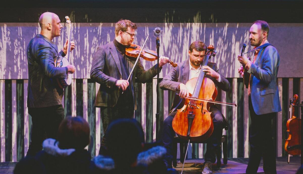 Four musicians on stage playing a banjo, violin, and cello