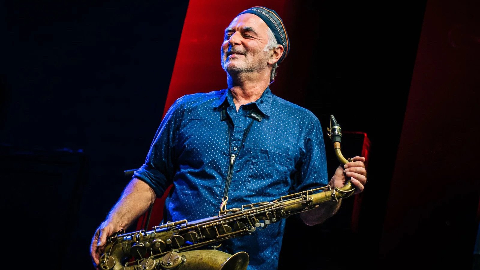 A man with grey hair wearing a blue button down holding a saxophone