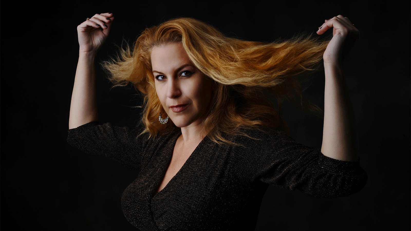 A woman wearing a black shirt throwing her light red hair back