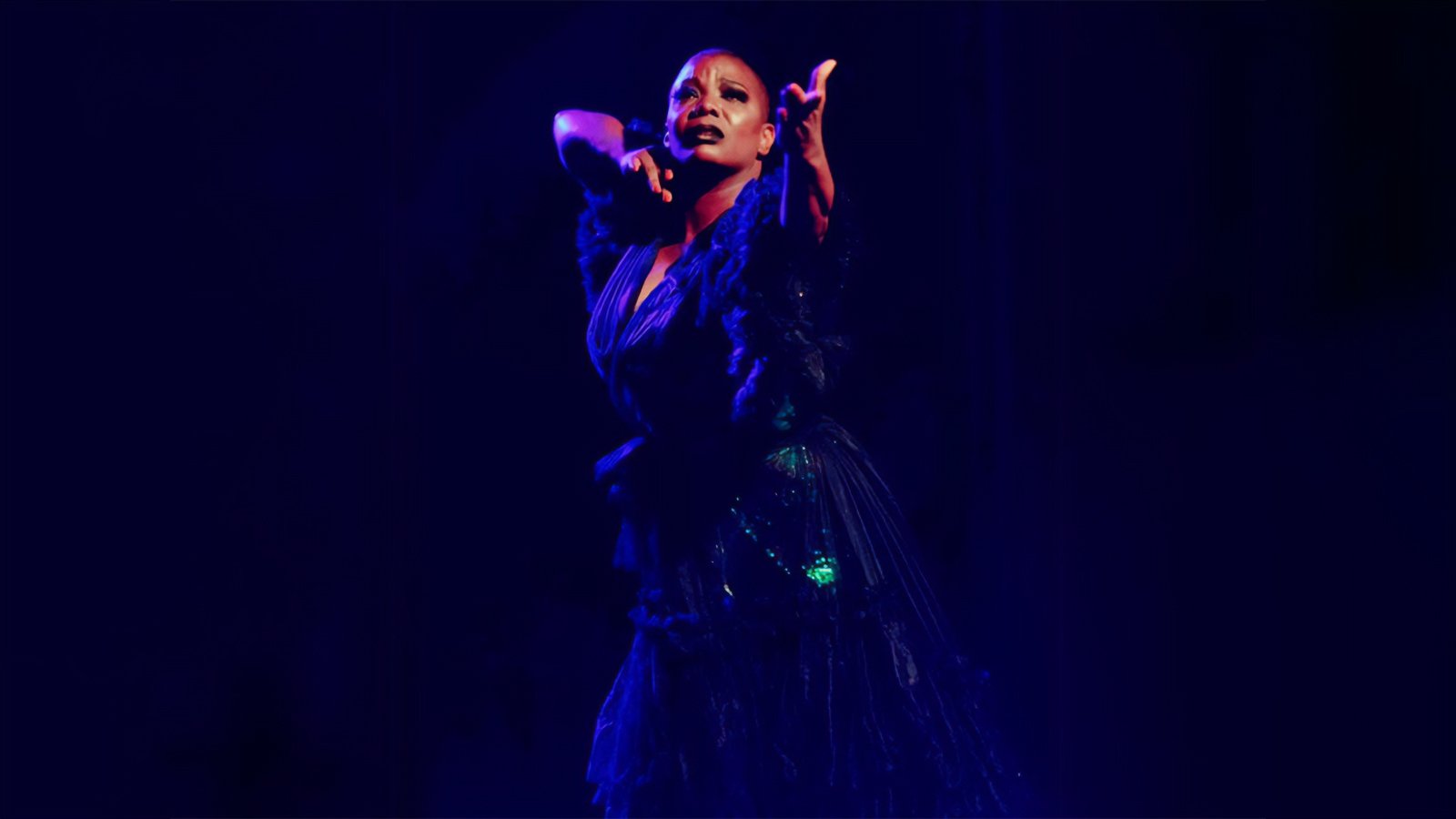 A black woman in a dark blue gown posing in dark overhead lighting