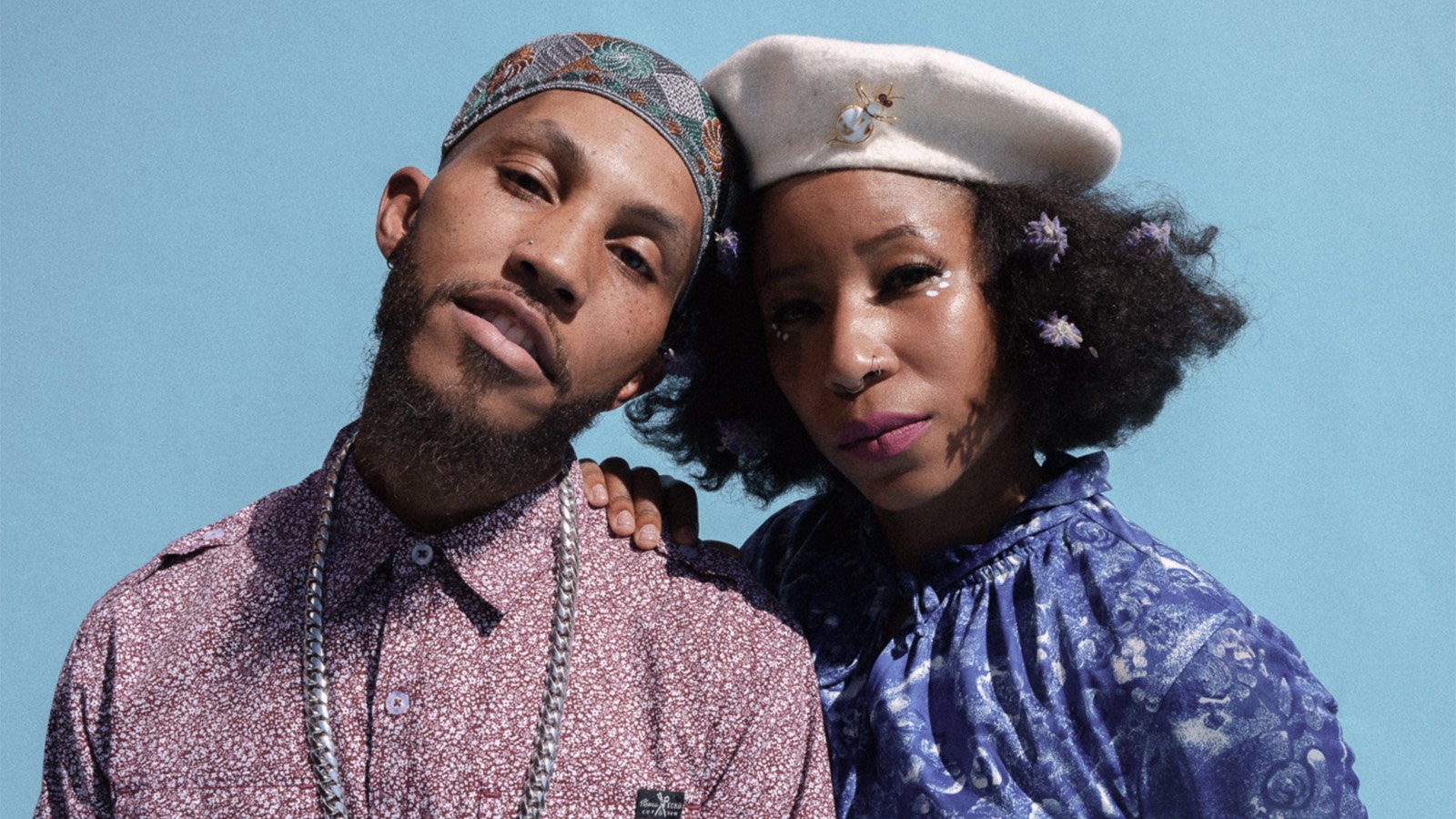 A black man in a purple shirt leaning his head against a black woman wearing a white hat and blue shirt 