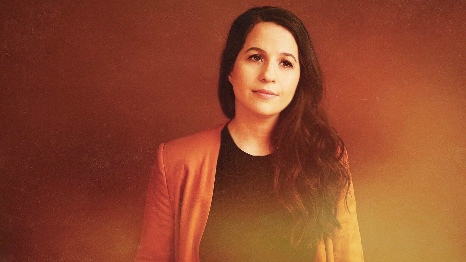A woman with long brown hair standing in an orange light