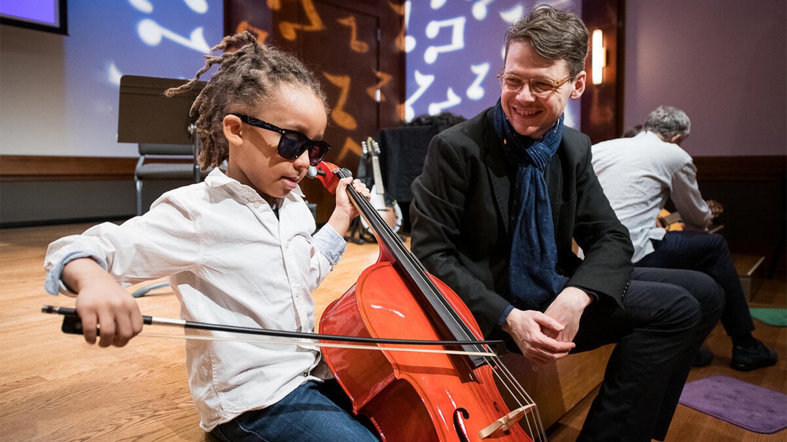 A child plays the violin while a CMS member directs them.
