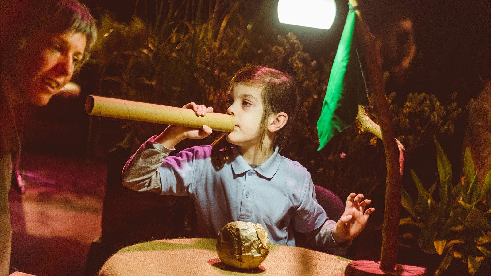A young child blows air through a cardboard flute