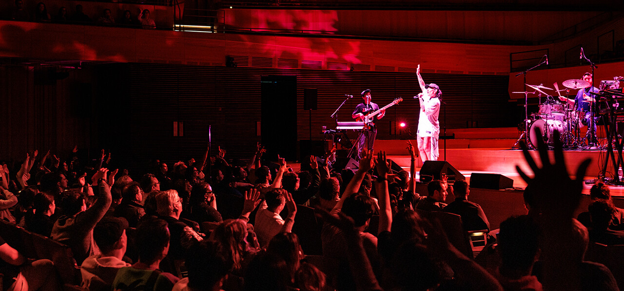 A woman with blond hair and a sparkly dress sings under a spotlight