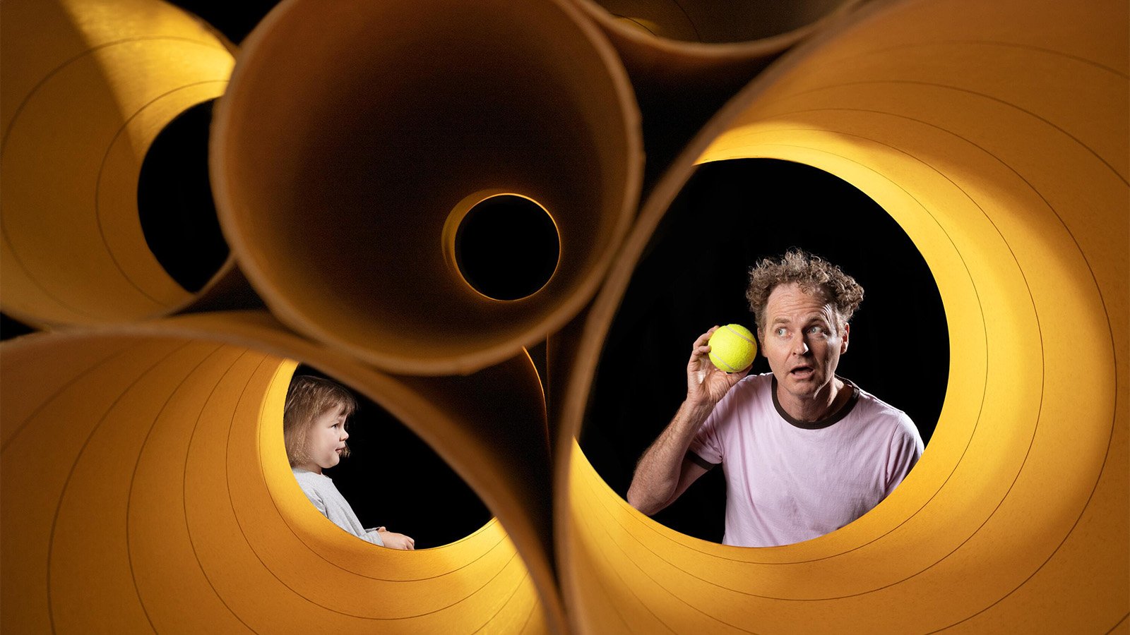 a girl watching a man listen to a tennis ball through paper towel holders