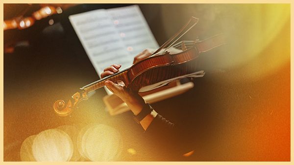 A musician plays a violin with sheet music in the background