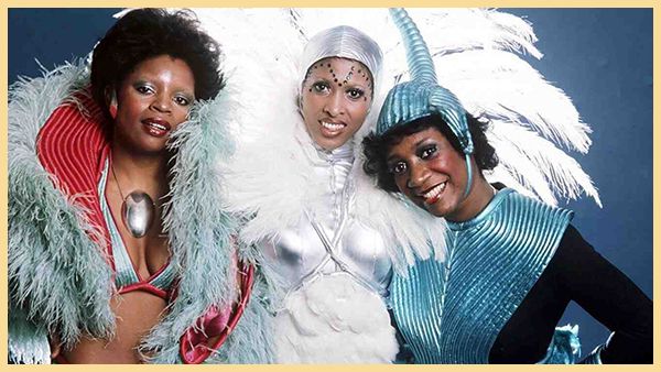 Members of the band Labelle wear feathered costumes and smile at the camera