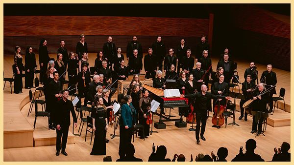 An orchestra stands on stage facing the audience