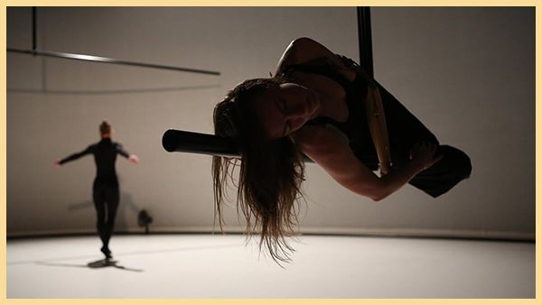 A dancer in the foreground rests on a metal bar while a dancer in the background stands on their toes.