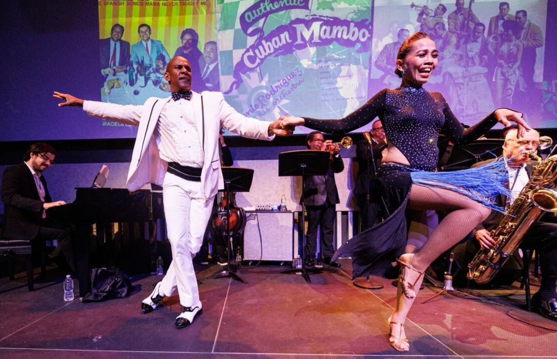 A man and woman in mambo costumes dance on stage
