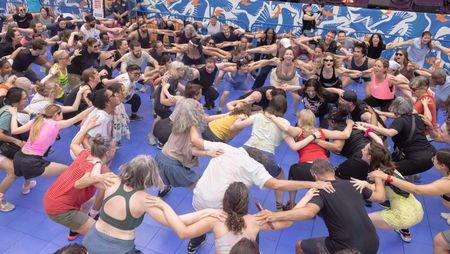 A crowd of people in circular formation link arms.