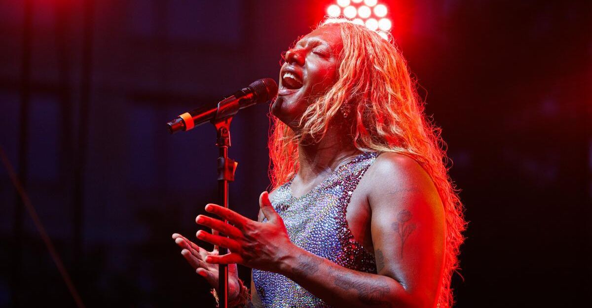 A woman stands under blue light, holding a guitar