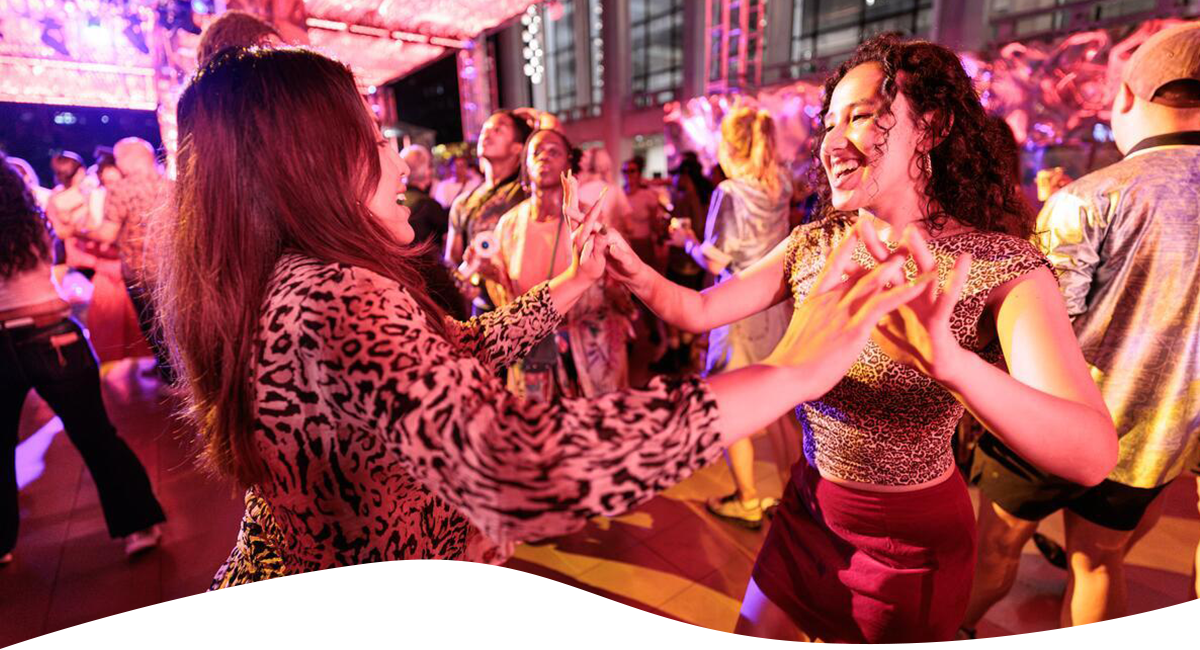 Two women dance hand-in-hand on a crowded dance floor