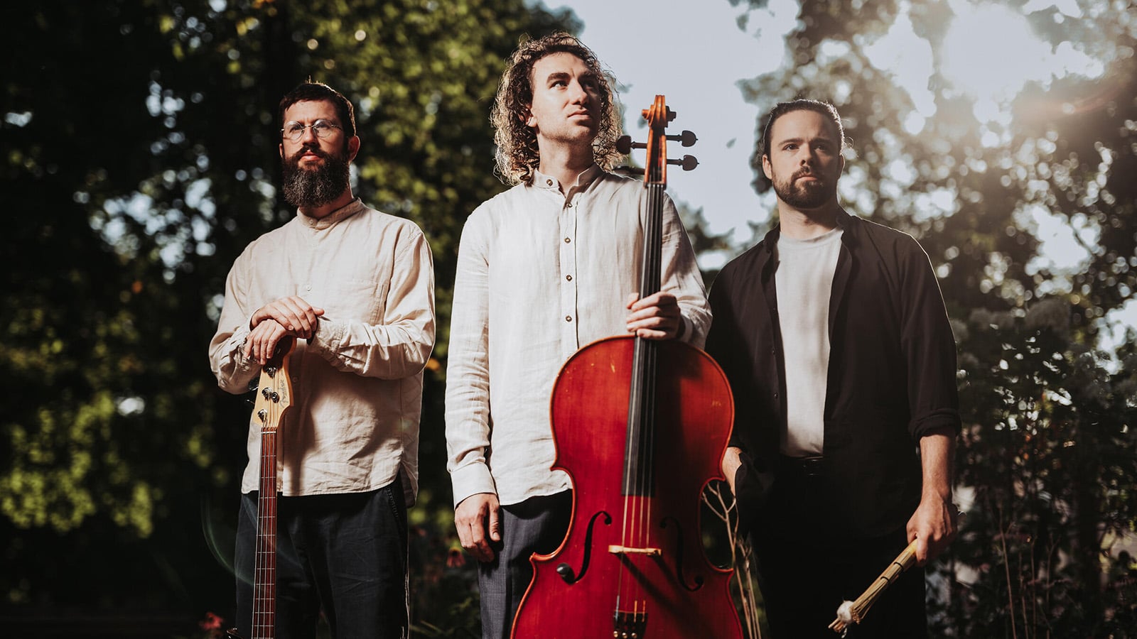 Three musicians hold instruments in an outdoor setting