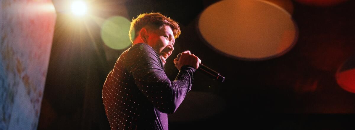 A man sings into a mic under spotlights