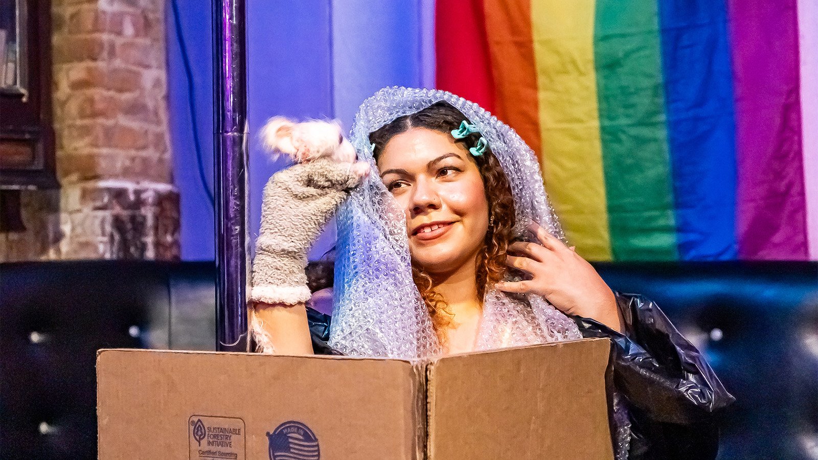A woman in a bubble-wrap veil holds up a puppet