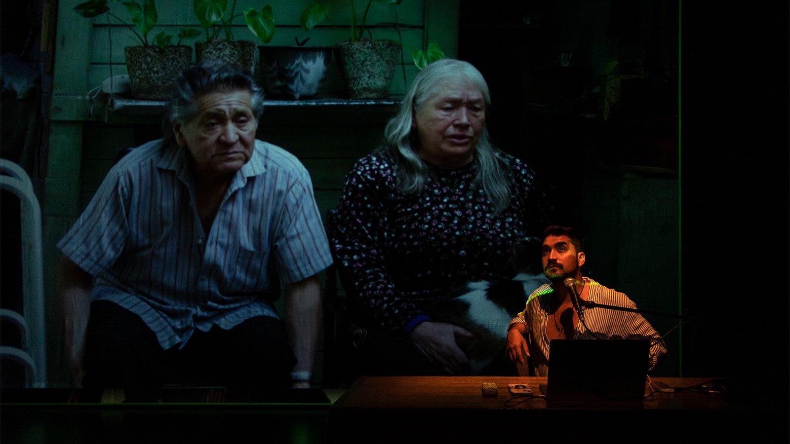 A man speaks into a microphone with an image on screen behind him