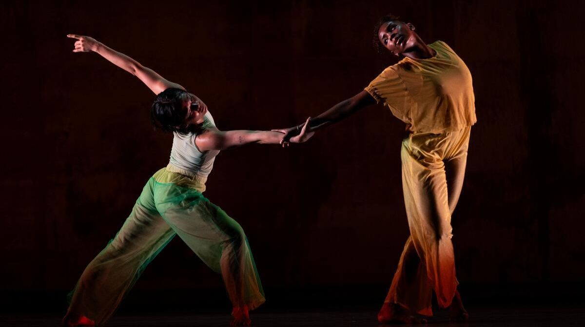 Two dancers lean into each other under dramatic lighting