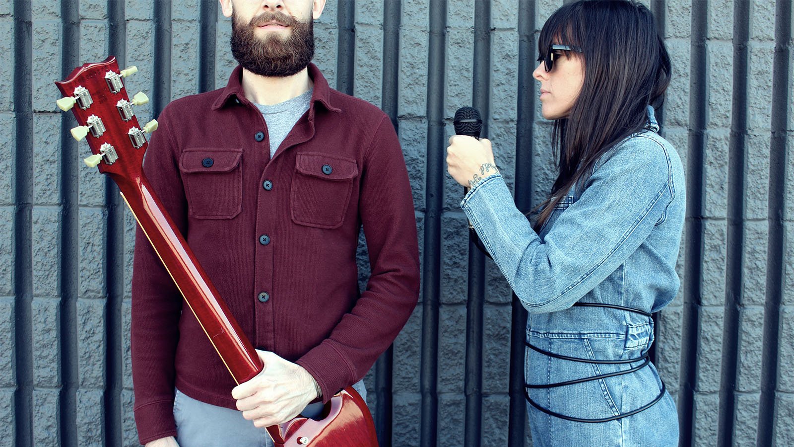 An image of Fusilier in a leather vest and a polo standing against a blue wall