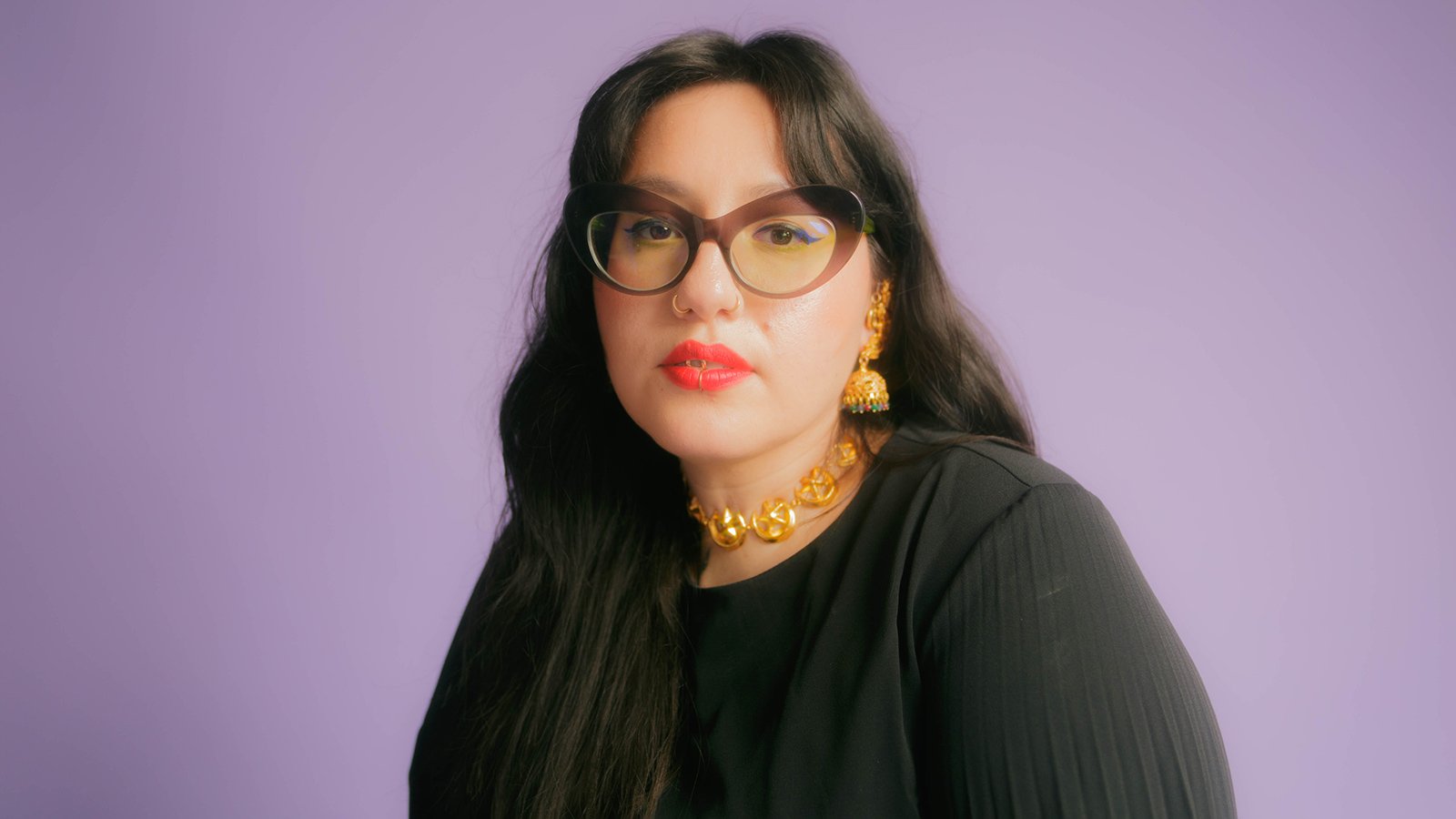 An image of Fusilier in a leather vest and a polo standing against a blue wall