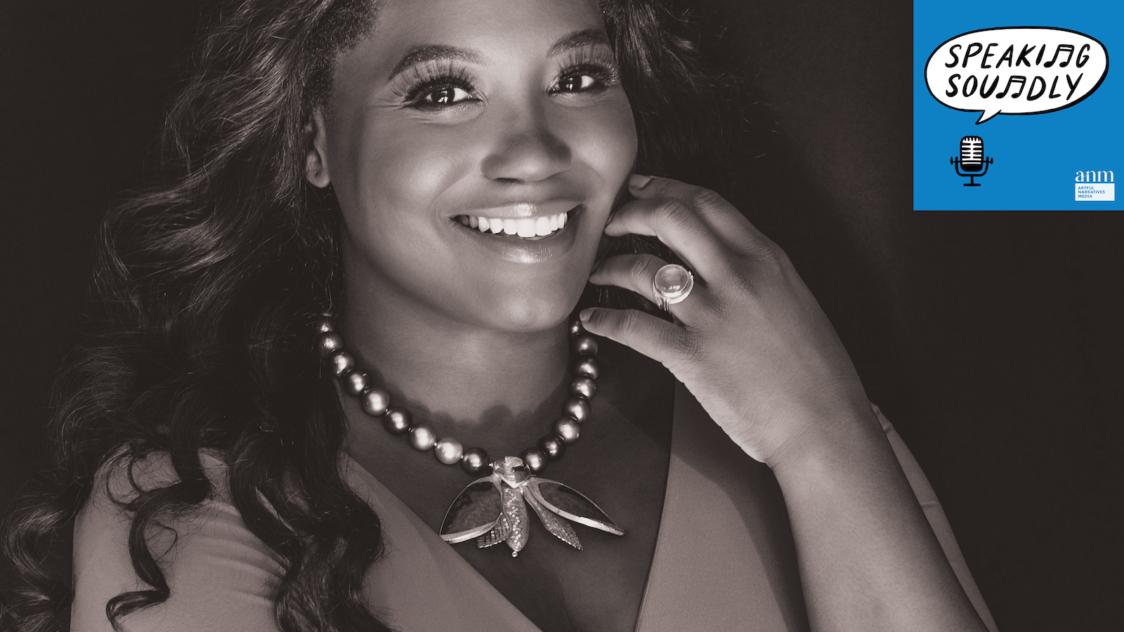 A black and white image of a woman with long dark hair wearing a metallic necklace