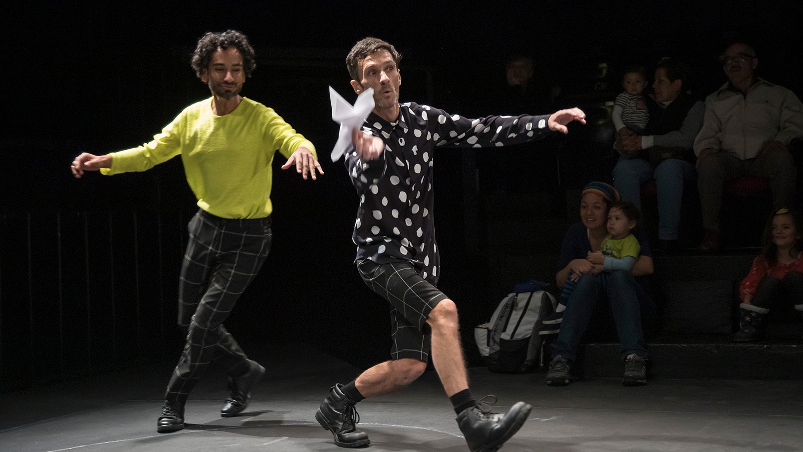 Two performers running across a stage holding a small paper bird