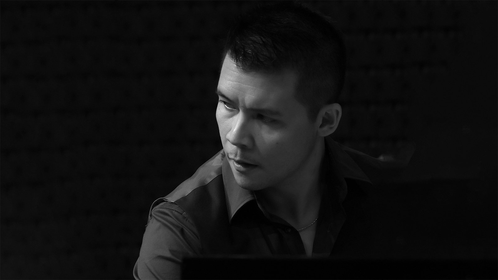 A black and white photo of a man with short dark hair wearing a collared shirt looking off to the side
