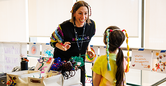 A teaching artist smiles at a child wearing a colorful costume