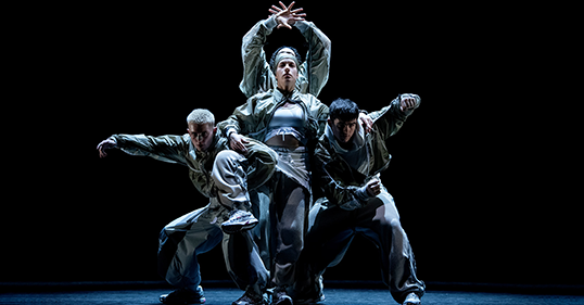 Dancers pose on stage in front of a black background