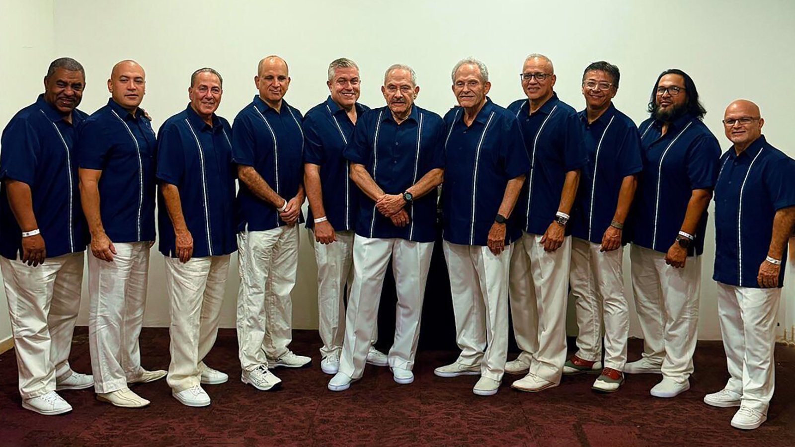 11 artists of Orquesta Broadway pose for a photo in blue shirts and white pants