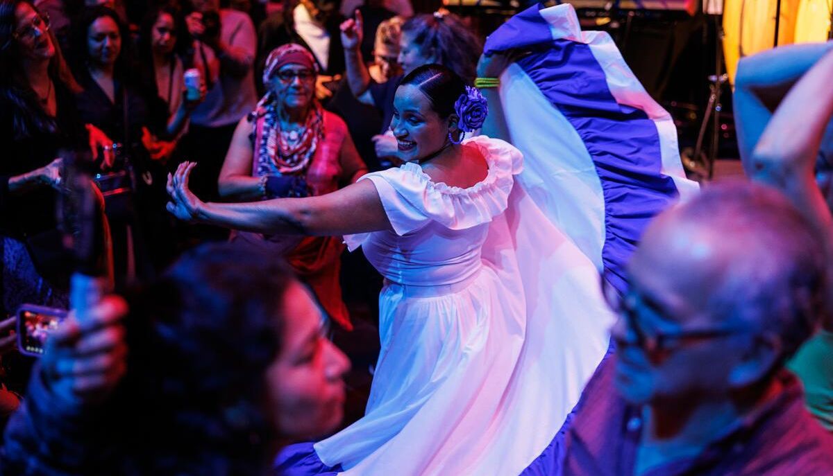 A woman in a long white dress with blue trim dancing in a crowd