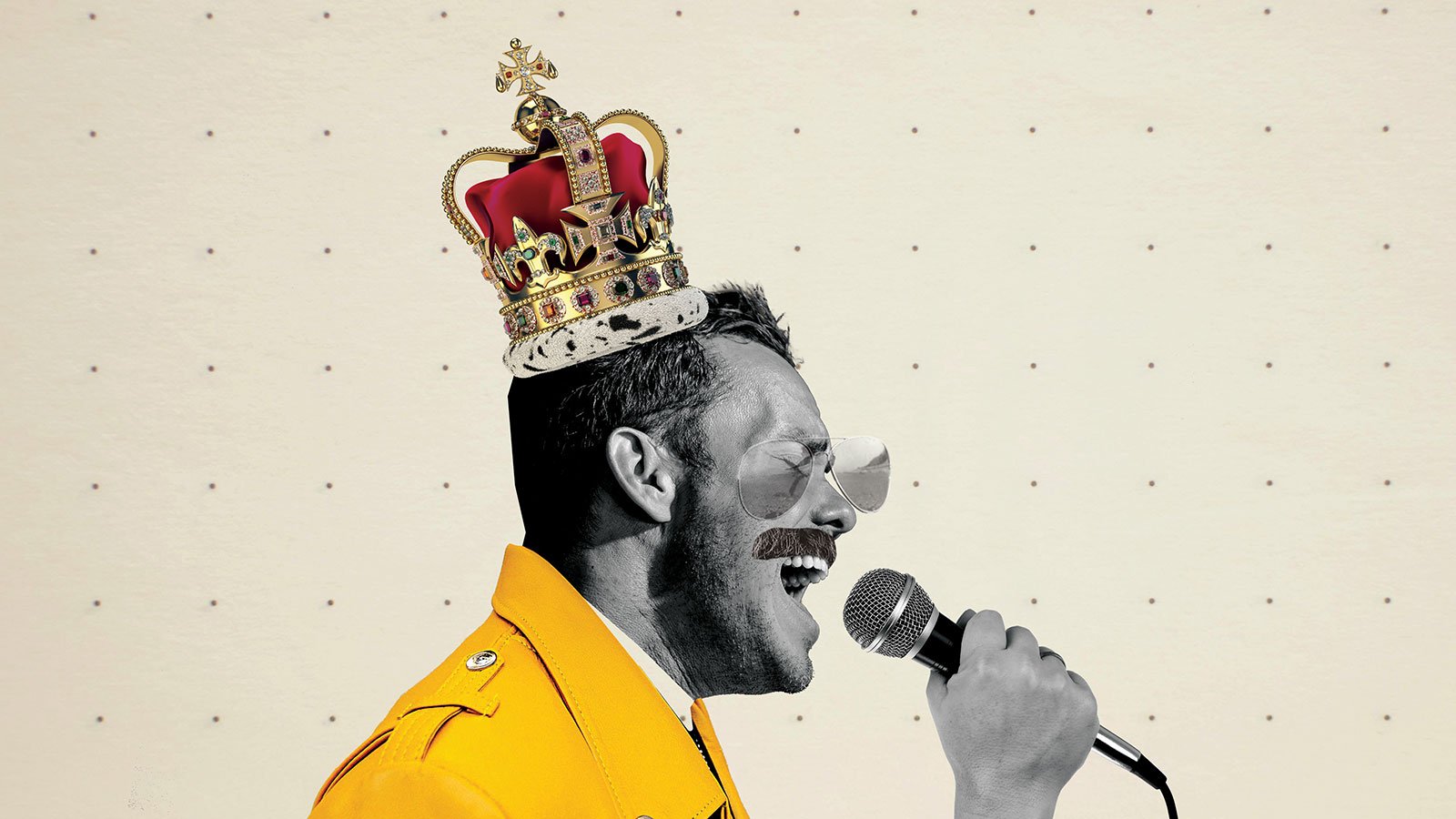 Photo of a man wearing a crown, glasses, and yellow jacket singing into a microphone