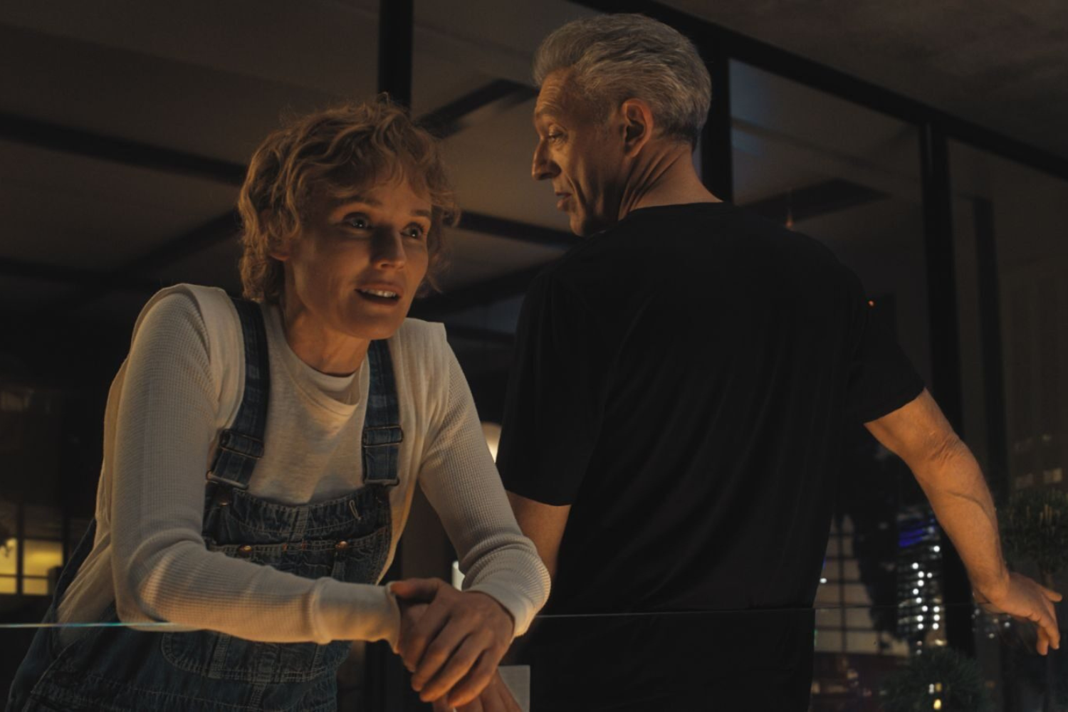 A woman in overalls talking to a man in a black t-shirt