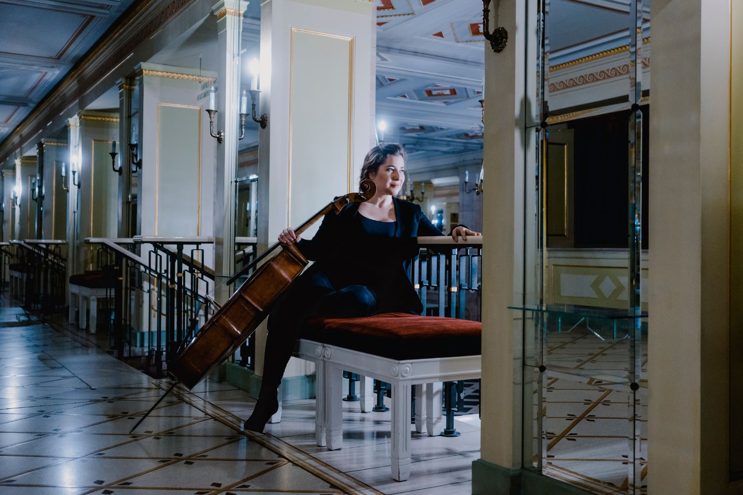 A woman sitting on a plush bench holding a cello