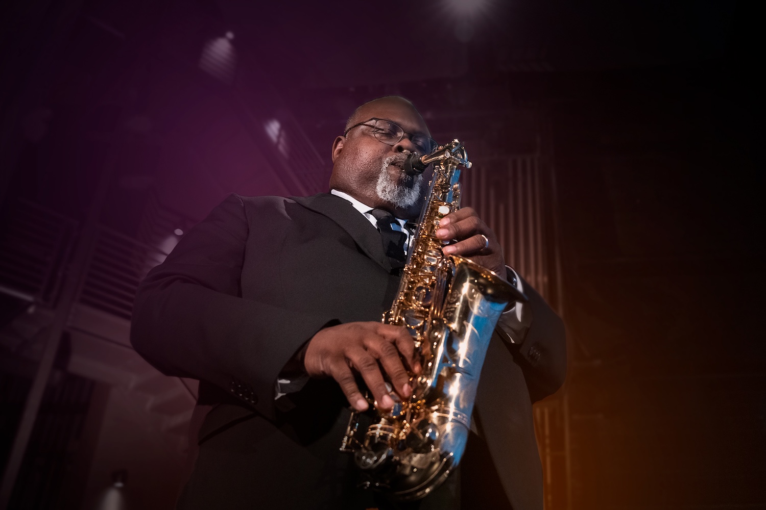A black and white photo of a woman with dark curly hair in front of a pink and blue graphic