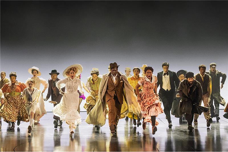A black and white photo of a woman with dark curly hair in front of a pink and blue graphic