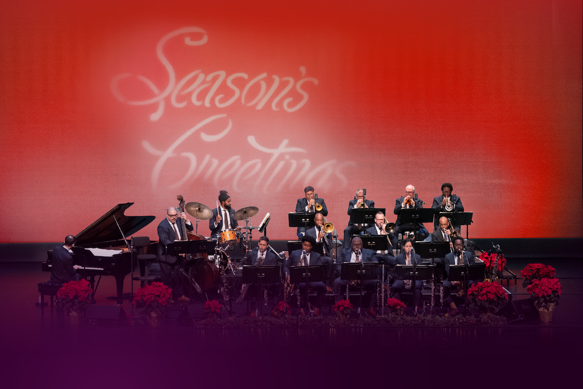 A black and white photo of a woman with dark curly hair in front of a pink and blue graphic