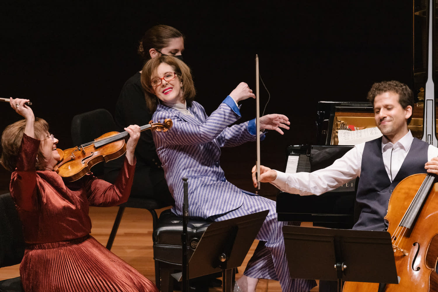 Four people performing on stage with a piano, violin, and cello