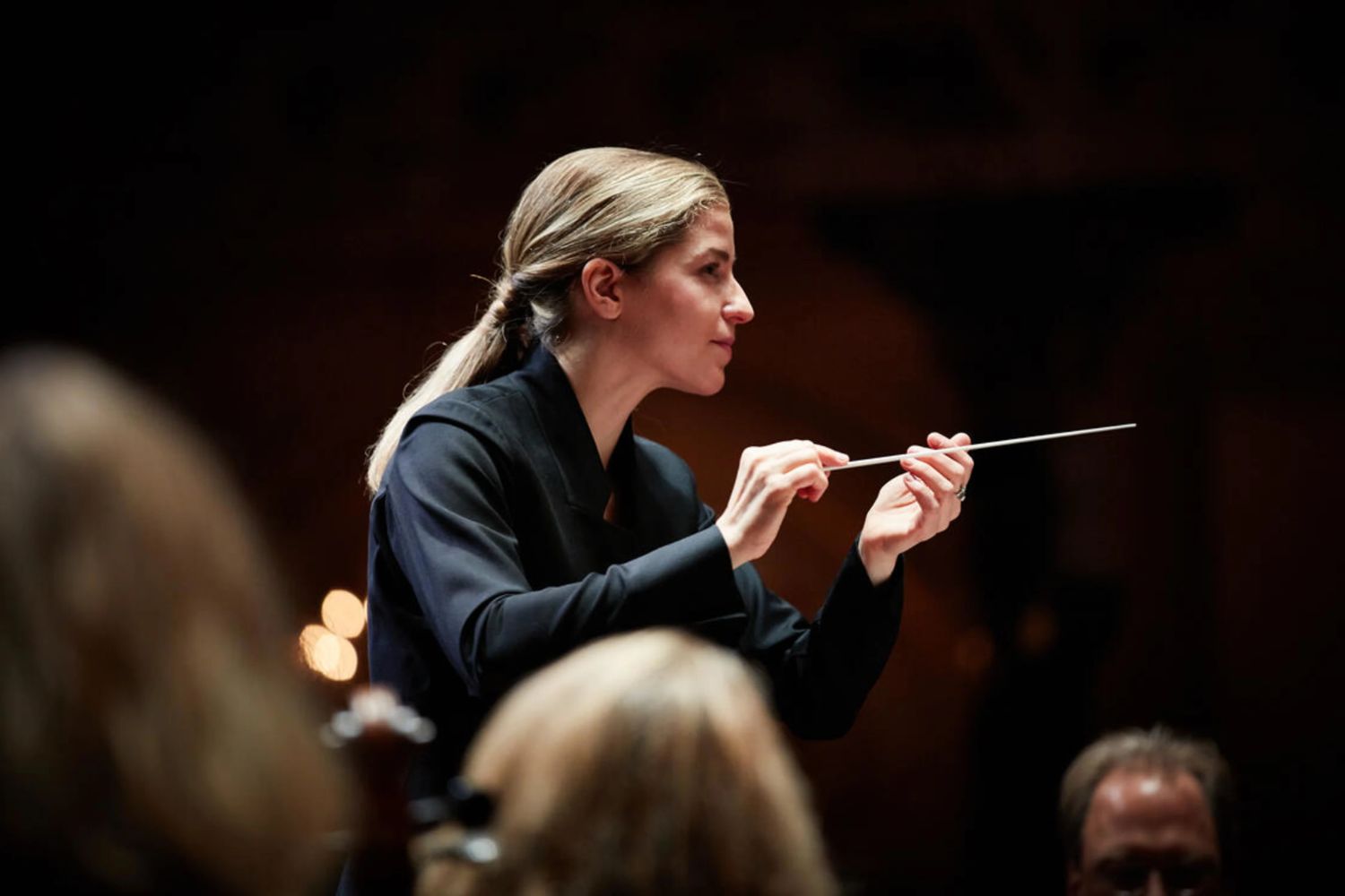 A woman in a black suit conducting an orchestra