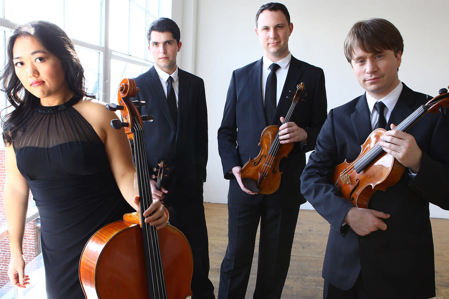 A woman in a black dress and three men in black suits posing with their string instruments