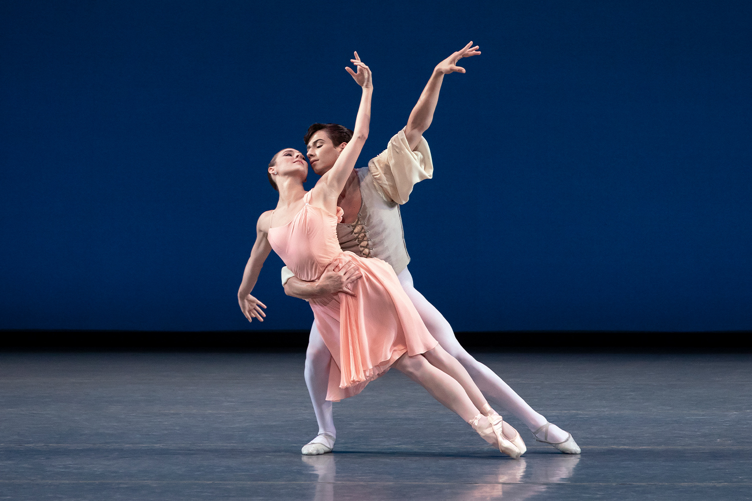 A ballerina in a pink dress being held by a male dancer in white tights