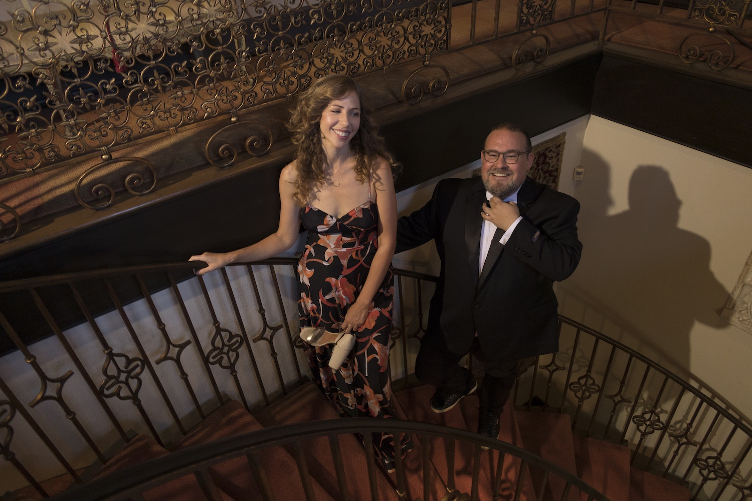 A woman in a floral dress and a man in a black suit standing on a spiral staircase